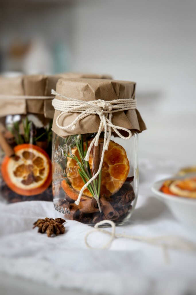 mason jars filled with dehydrated orange slices star anise, cinnamon and rosemary sprigs. Wrapped on top with brown paper and held with twine.