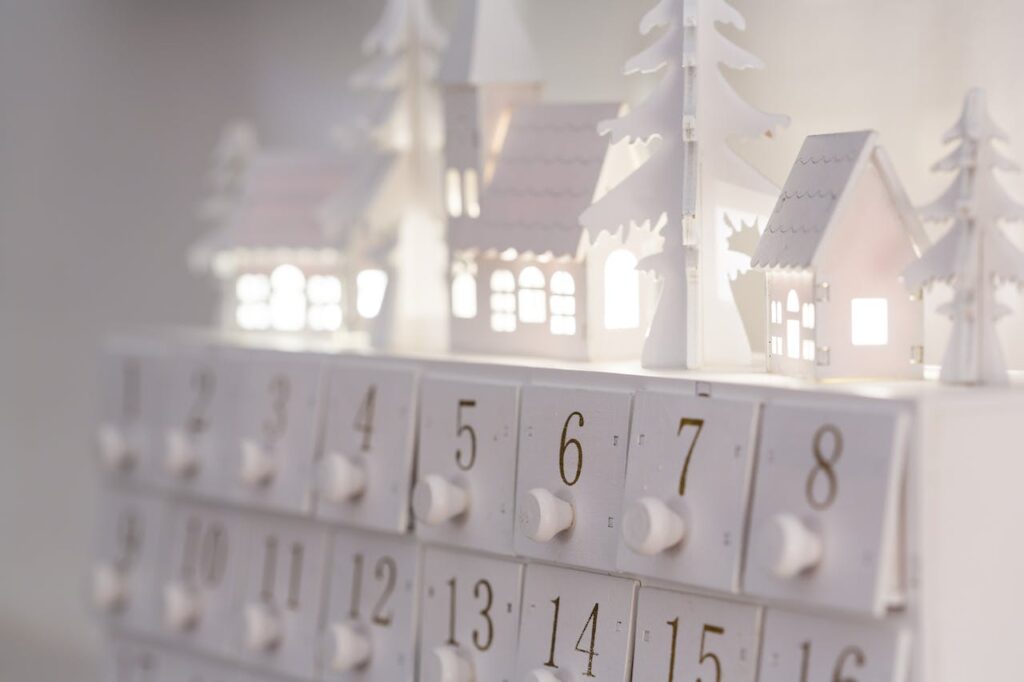 White advent calendar with doors and knobs for each day topped with lit Christmas village model